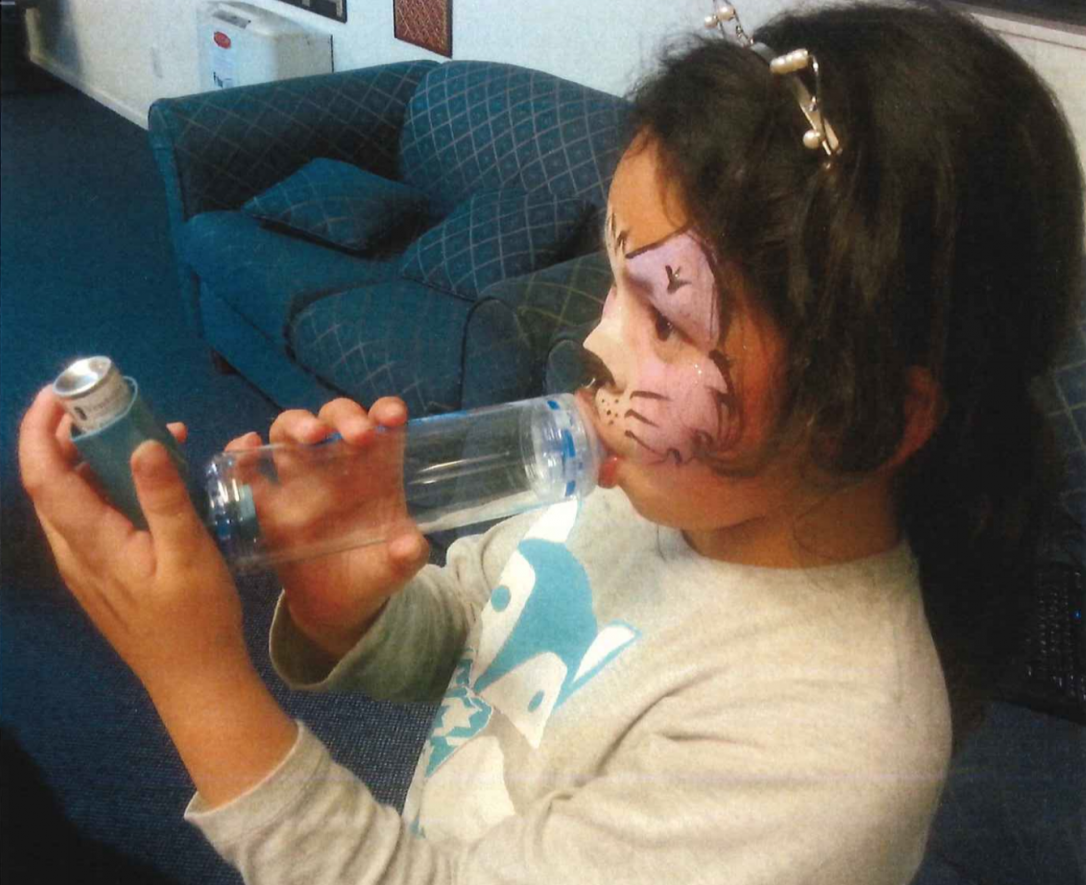 Young girl using an asthma inhaler with a spacer